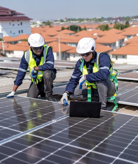 Engineer on rooftop kneeling next to solar panels photo voltaic check laptop for good installation